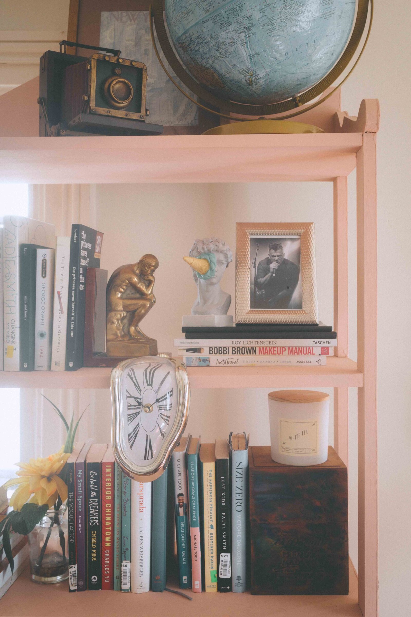 bohemian bookshelf decor with vintage camera, globe, books, candle, and styled art objects in a cozy eclectic home