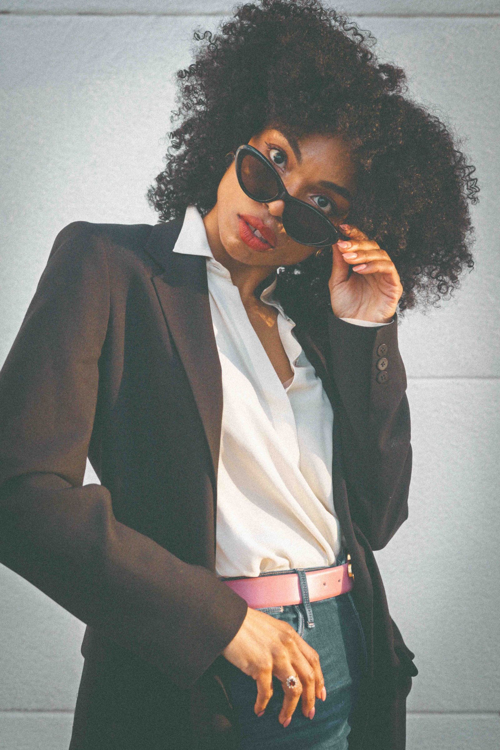 Black woman in black blazer looking over cat eye sunglasses, close up editorial portrait, style confidence