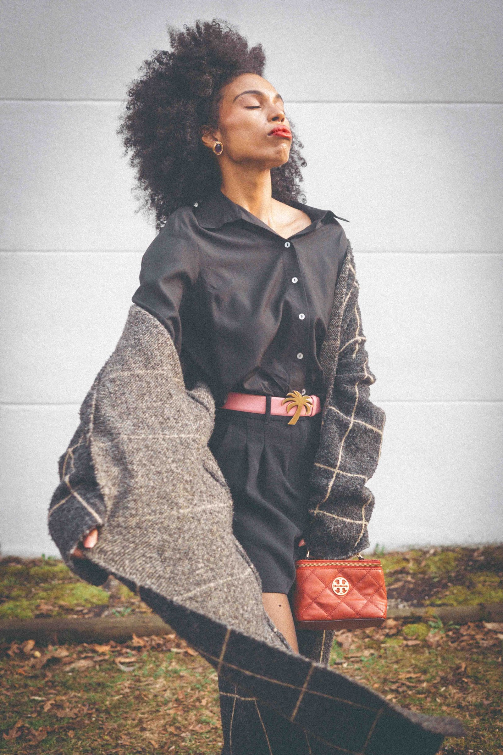 Black woman in plaid cardigan with eyes closed, Tory Burch quilted bag, intentional dressing editorial portrait