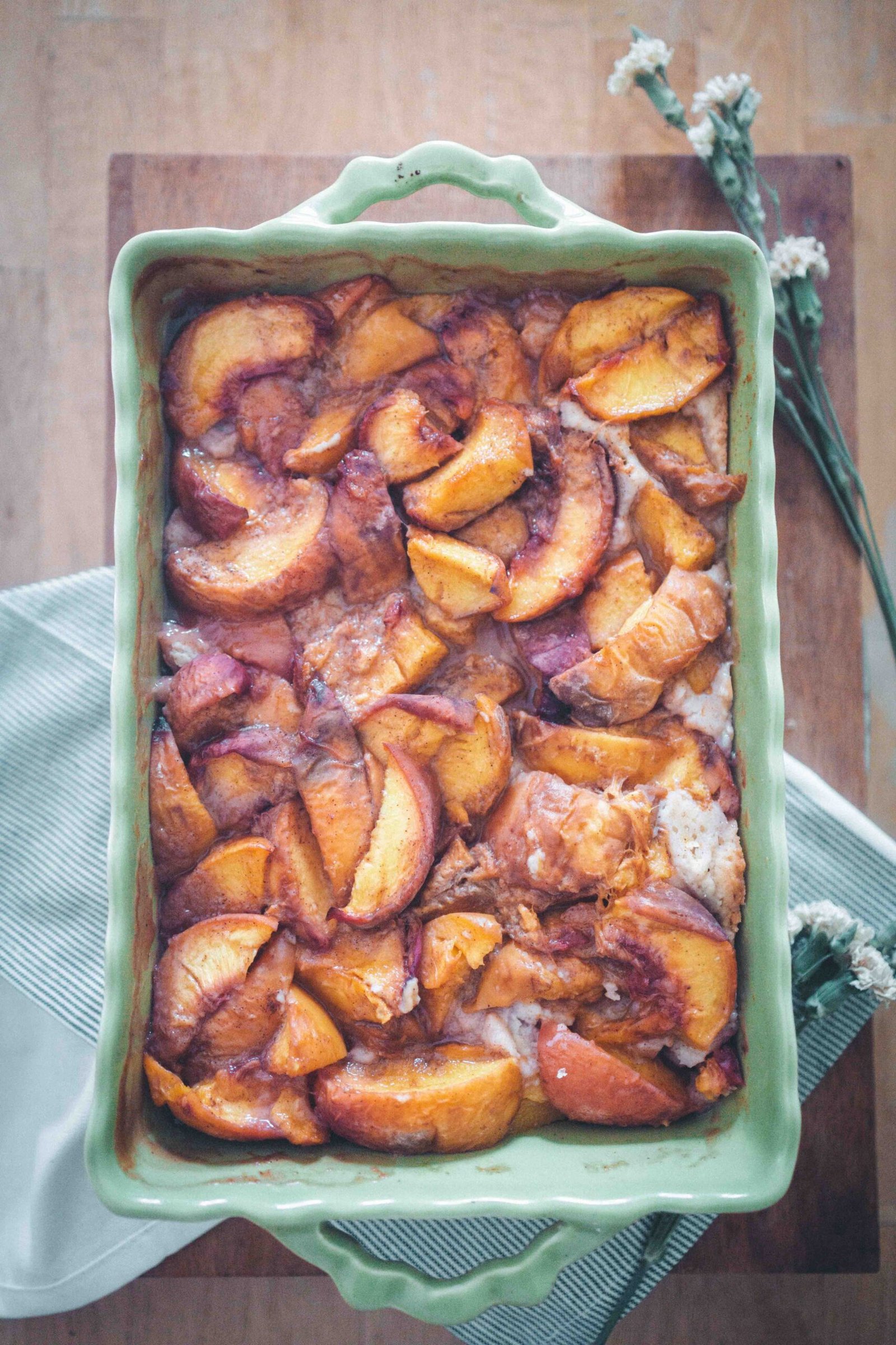Freshly baked brown butter peach cobbler with cinnamon-spiced peaches in a green baking dish.