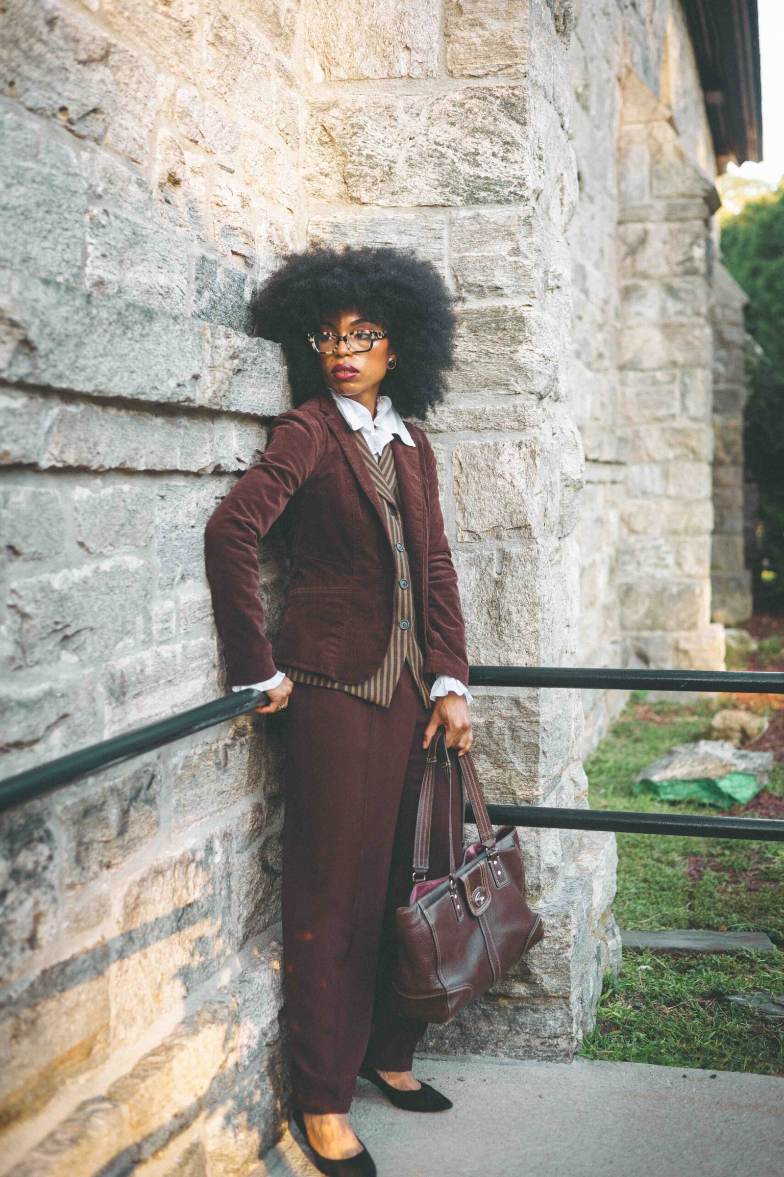Full-length portrait of a woman in a brown corduroy blazer, striped waistcoat and wide-leg trousers