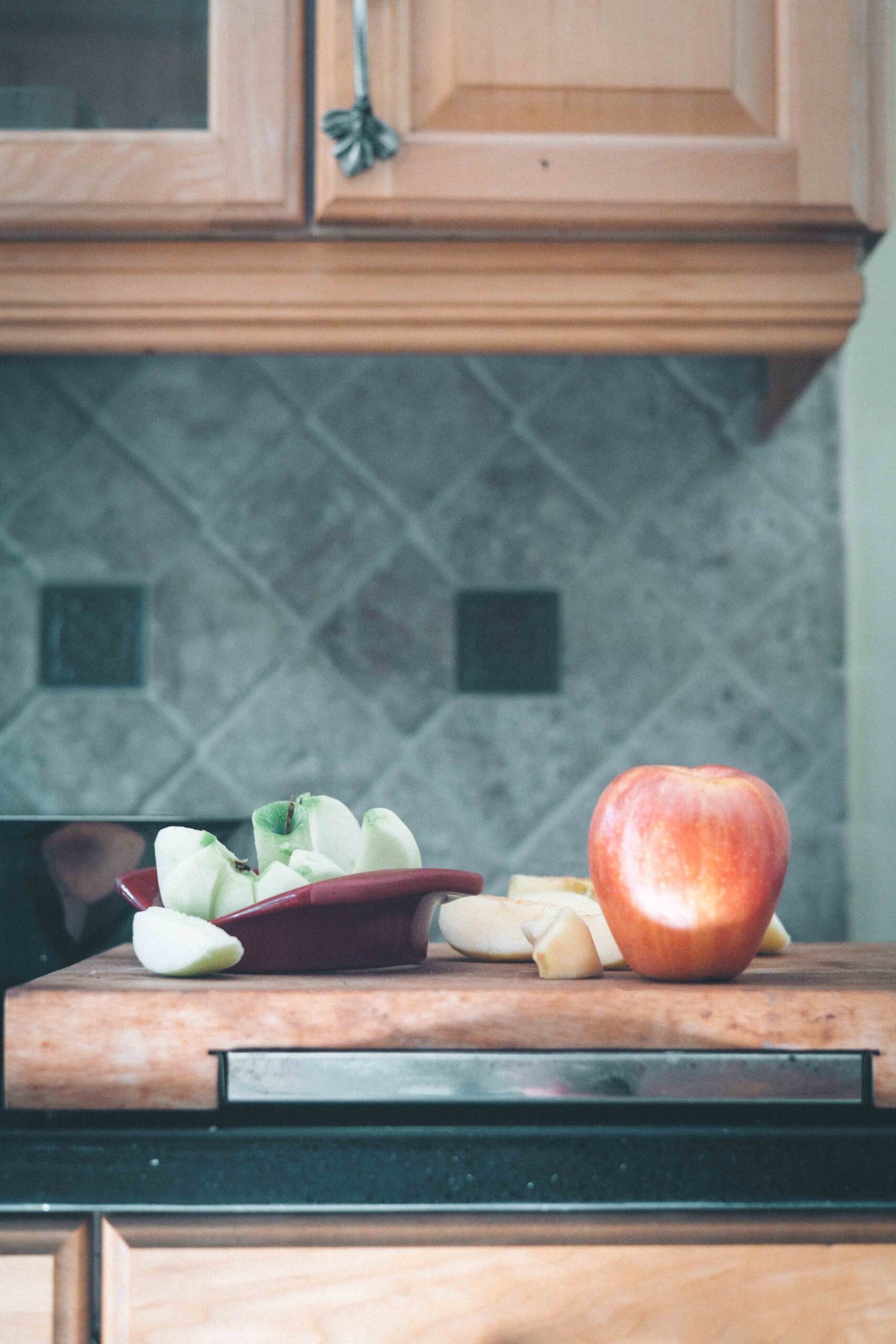 Chopped apples and a whole red apple arranged on a wooden cutting board during cake preparation.