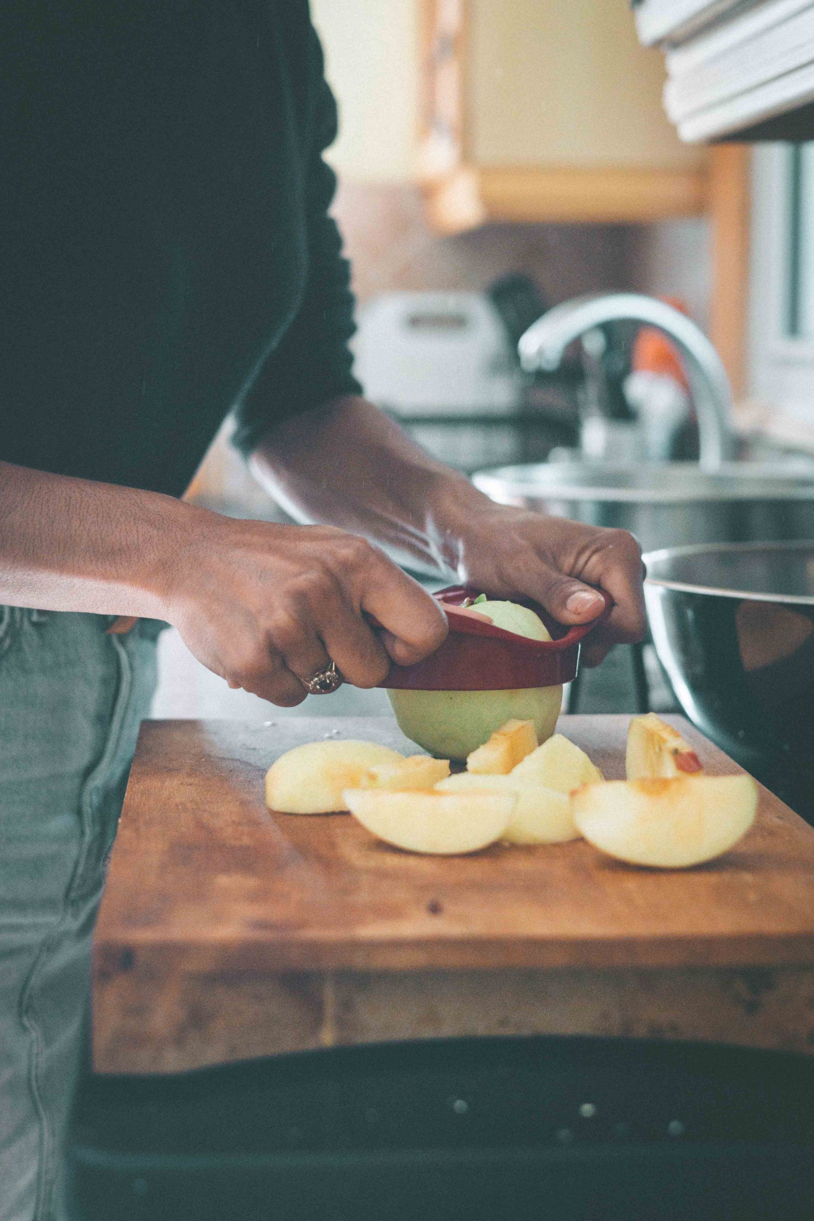 Hands coring a peeled green apple on a wooden cutting board with apple wedges nearby.