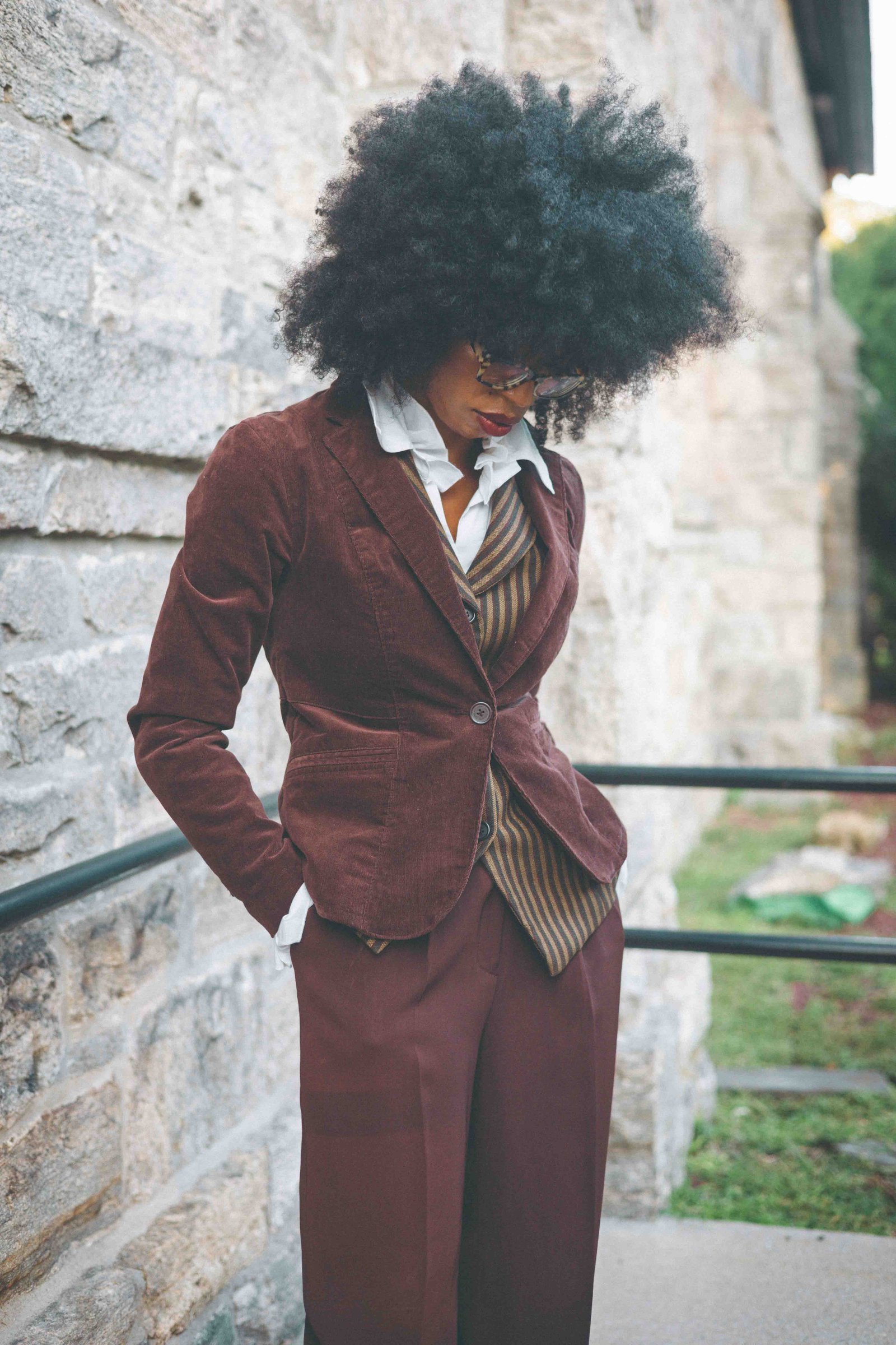 Detail of a brown corduroy blazer layered over a striped wool waistcoat and white poet blouse