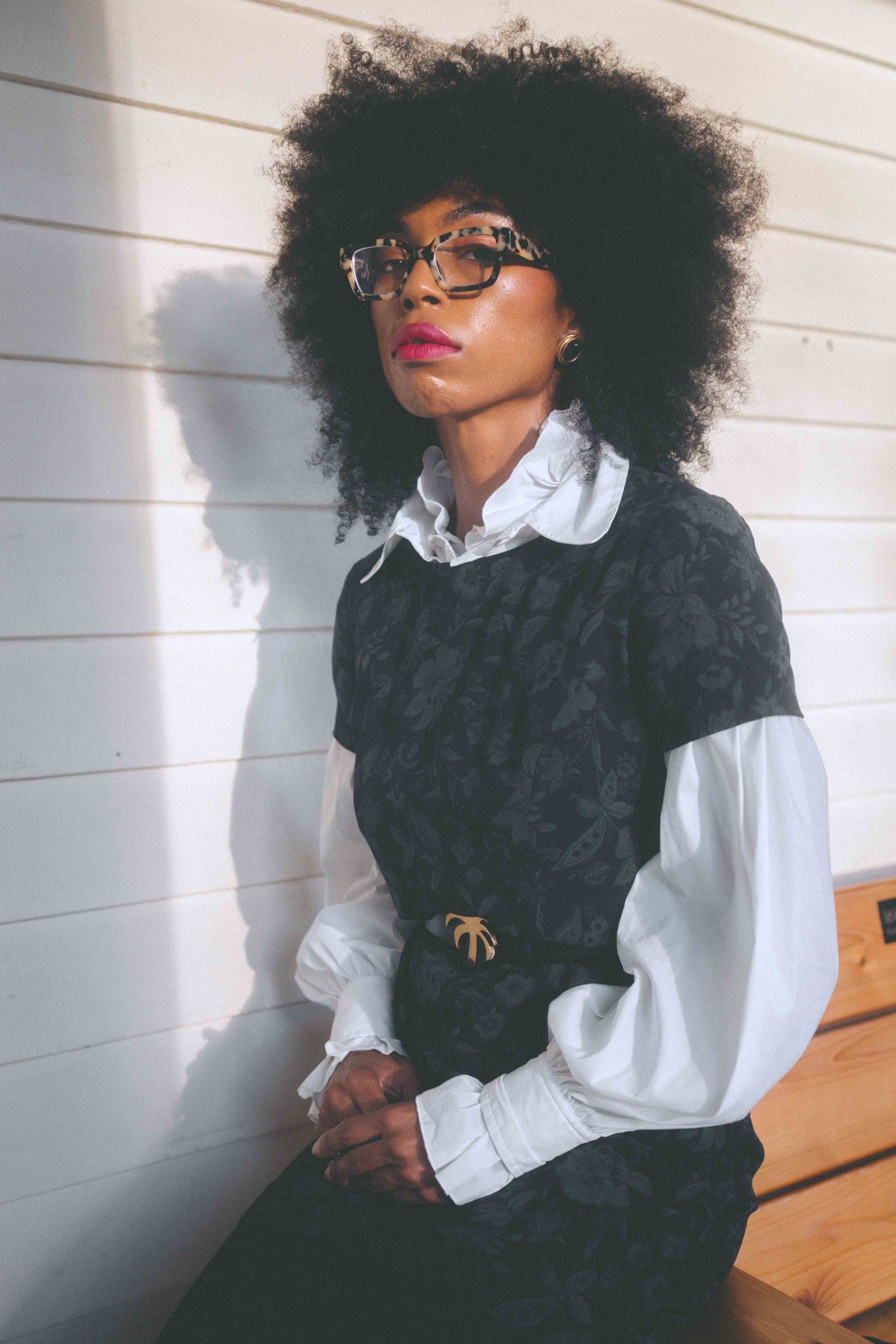 Sunlit seated portrait of a woman wearing a vintage dark floral dress and white poet blouse
