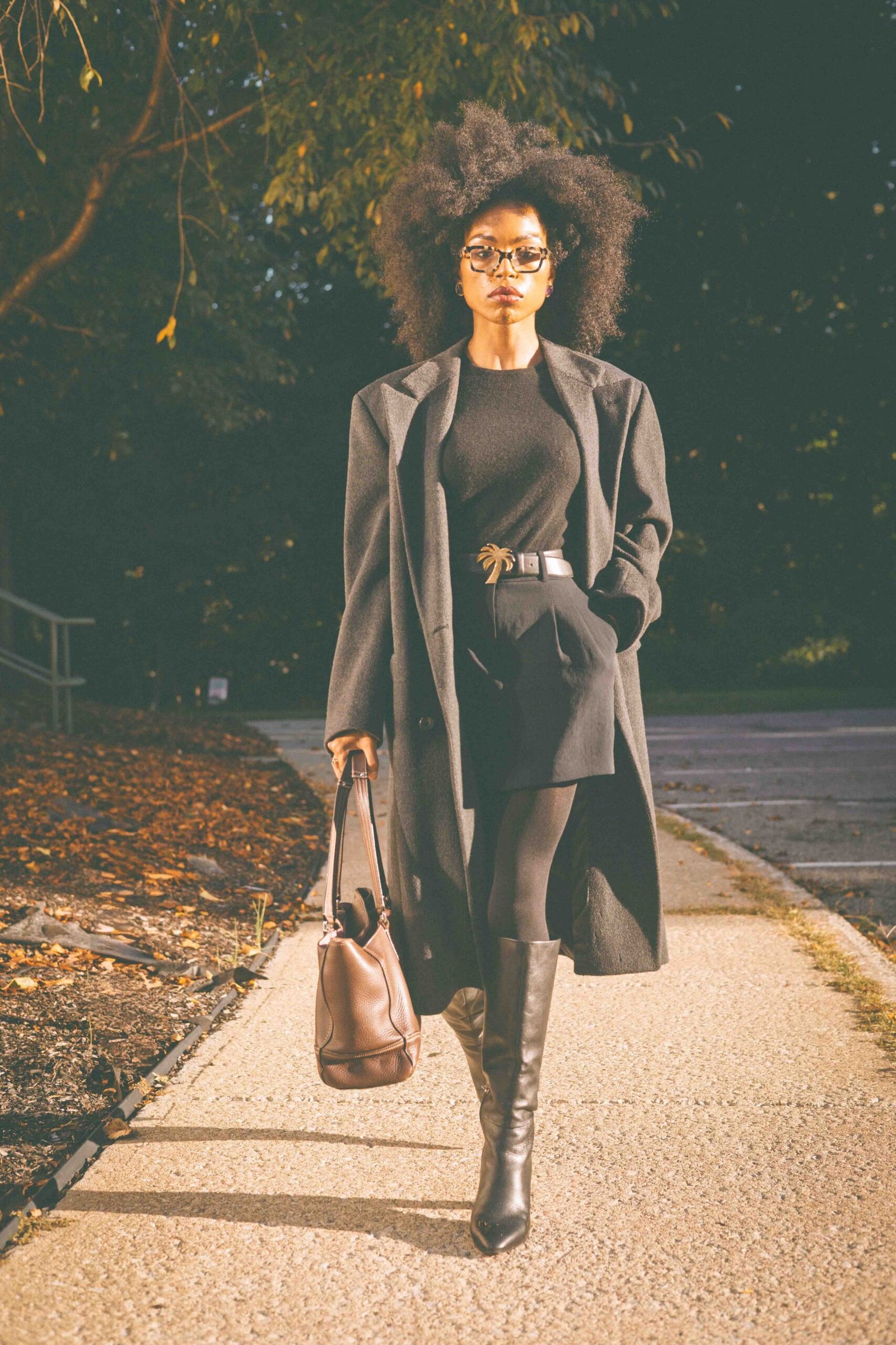 Inspired by Fall 2026 fashion trends, woman walks in a black fall outfit with an oversized charcoal wool coat and knee-high boots. 