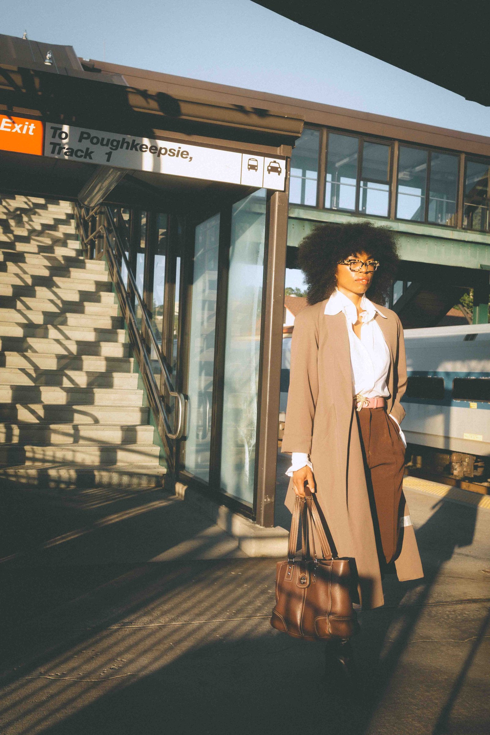 Woman in a vintage taupe trench coat and chocolate trousers standing on a train platform