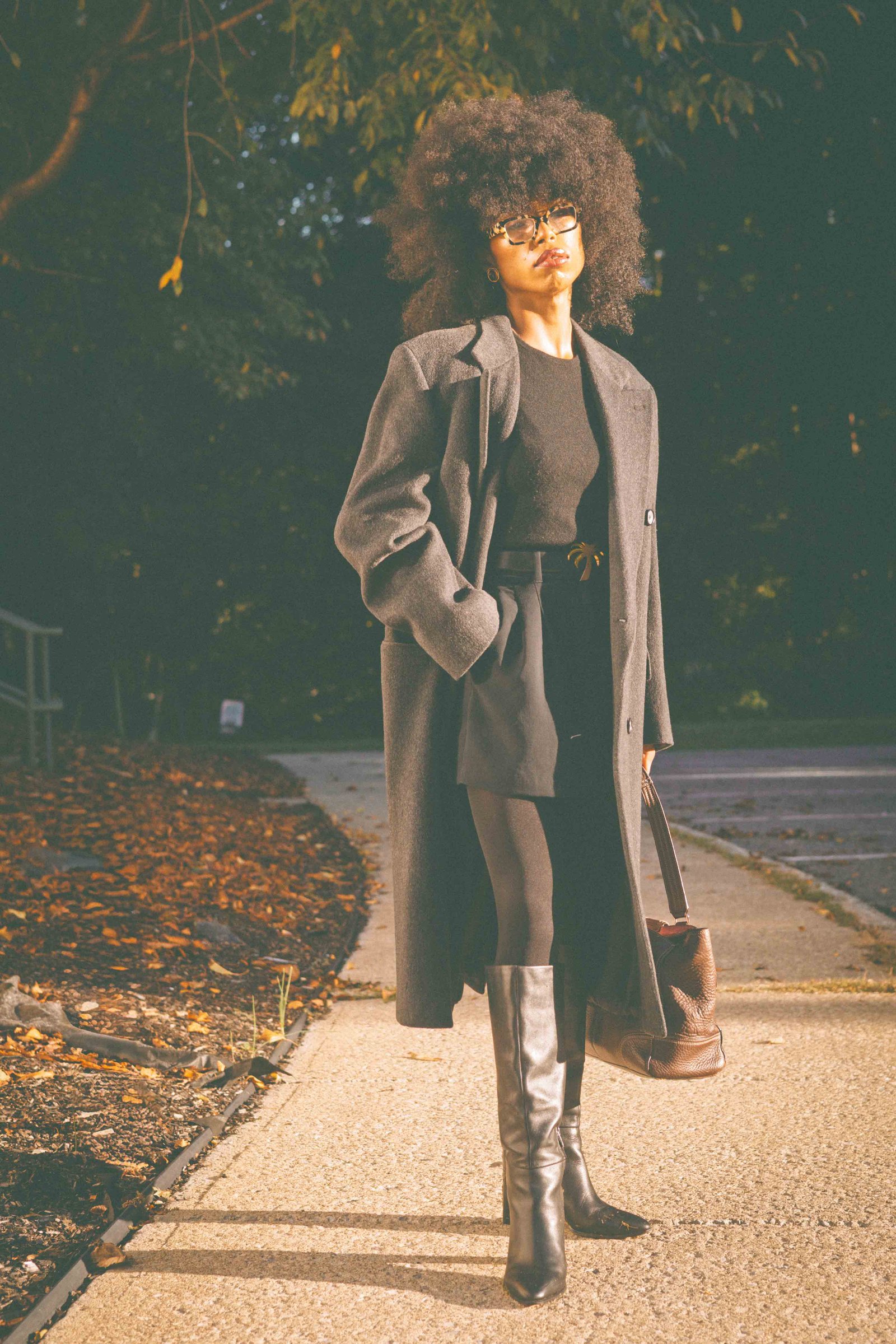 Woman posing in an oversized charcoal wool coat against a sunlit exterior wall