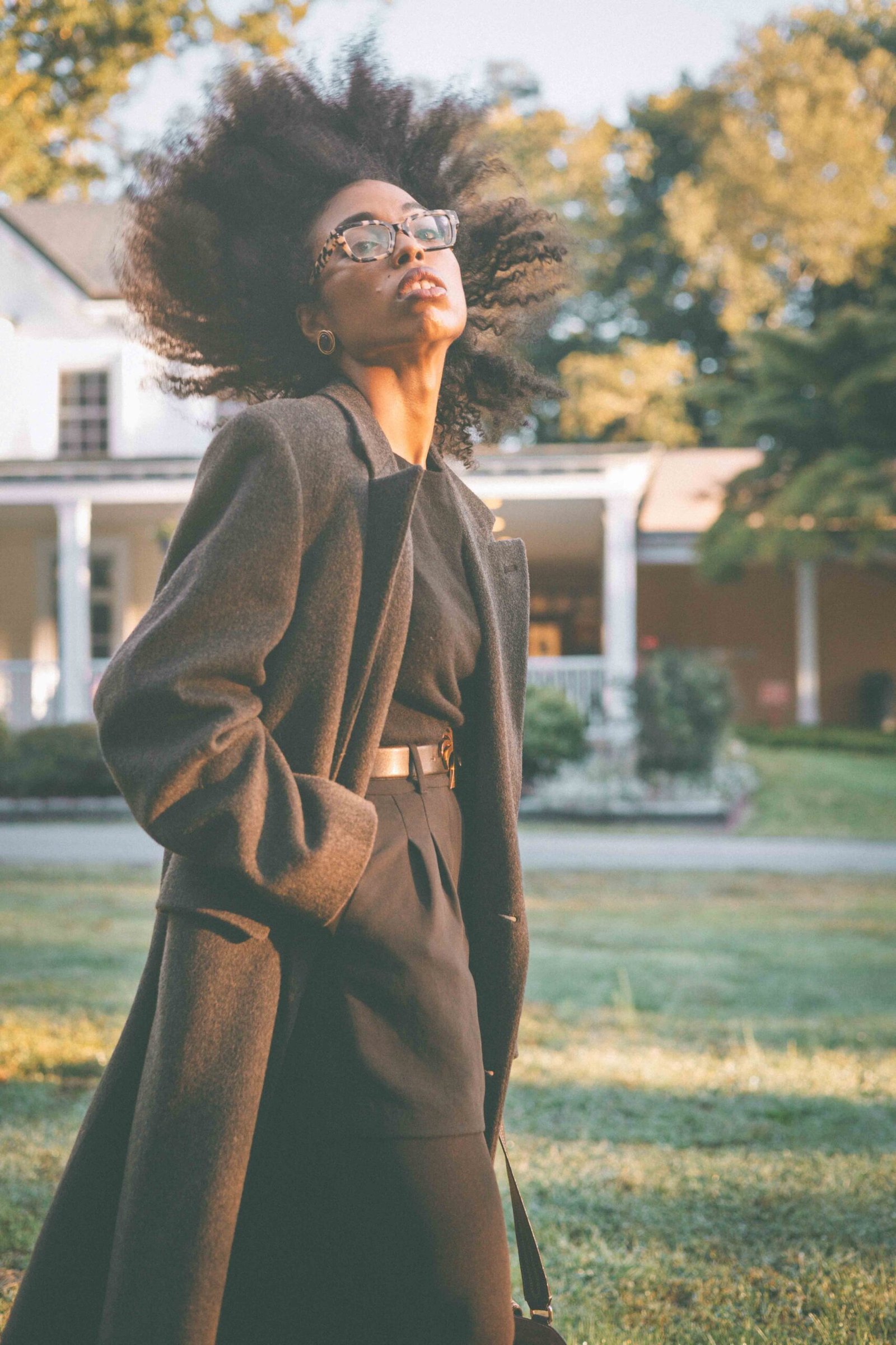 Low-angle portrait of a woman wearing an oversized charcoal wool coat over a black cashmere sweater and mini skirt