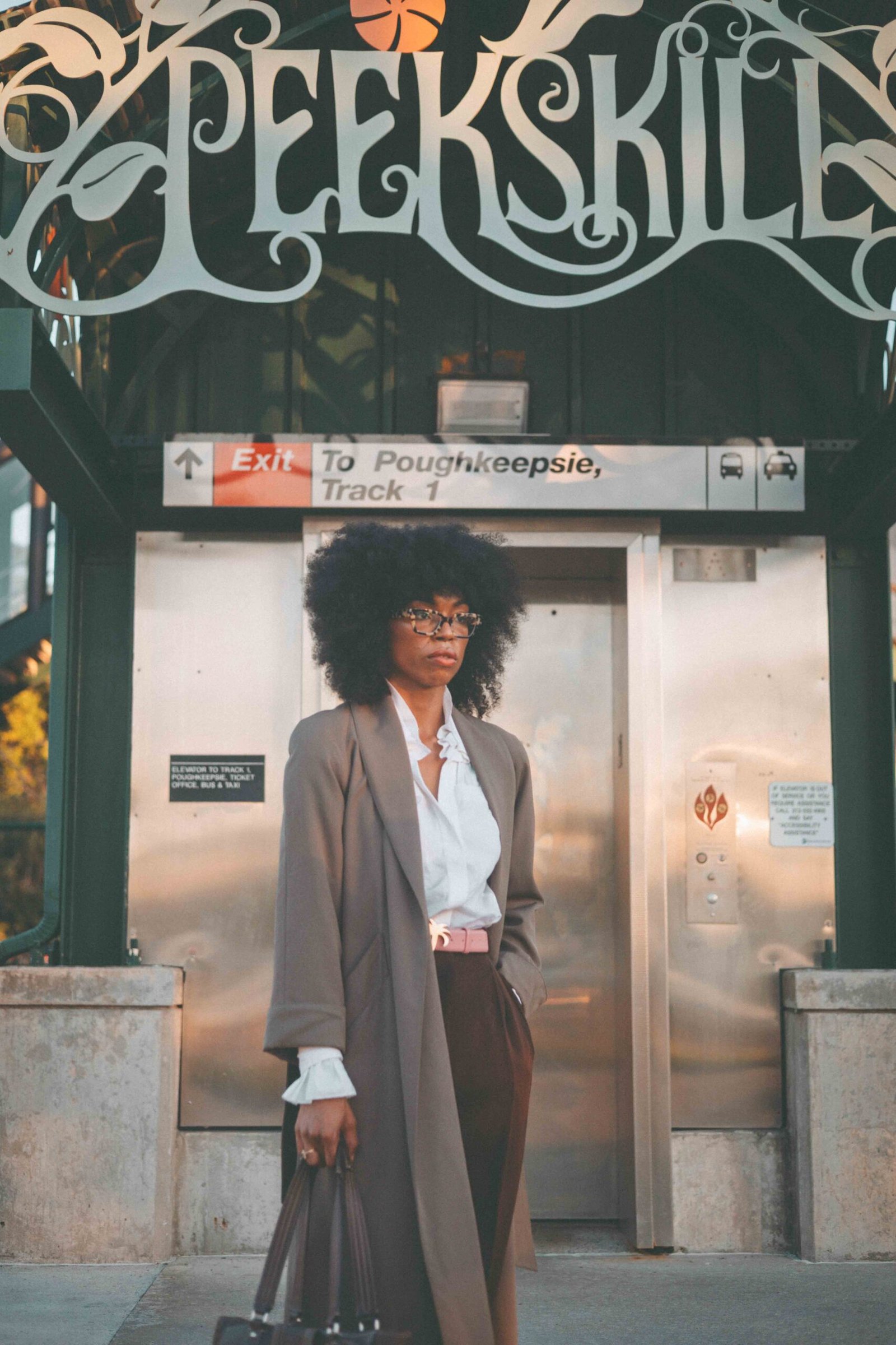 Woman in a white poet blouse and tailored brown trousers standing outside Peekskill station