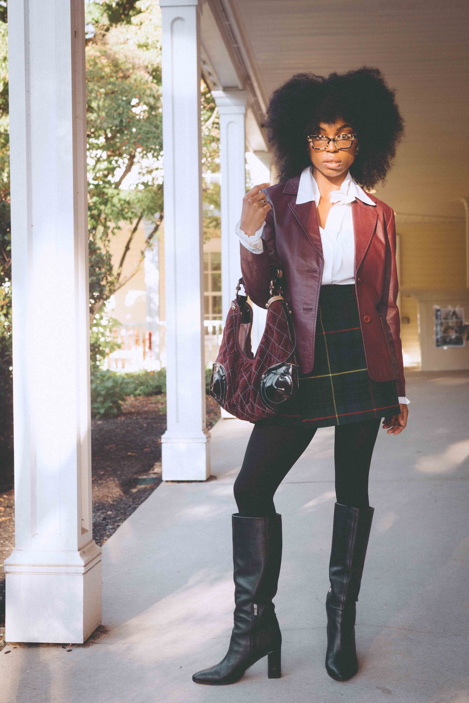 Early morning porch portrait in a burgundy leather blazer, plaid skirt and knee-high boots