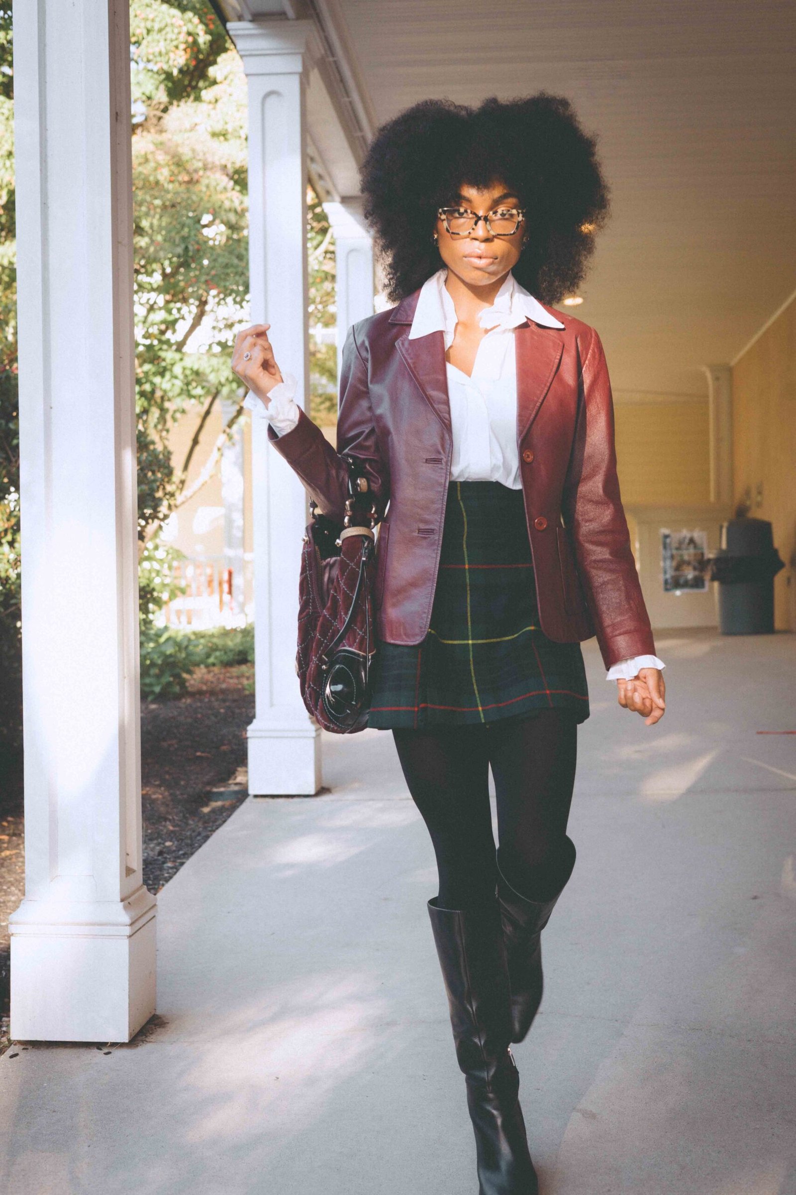 Woman walking in early morning light wearing a vintage burgundy leather blazer and Scottish wool plaid skirt