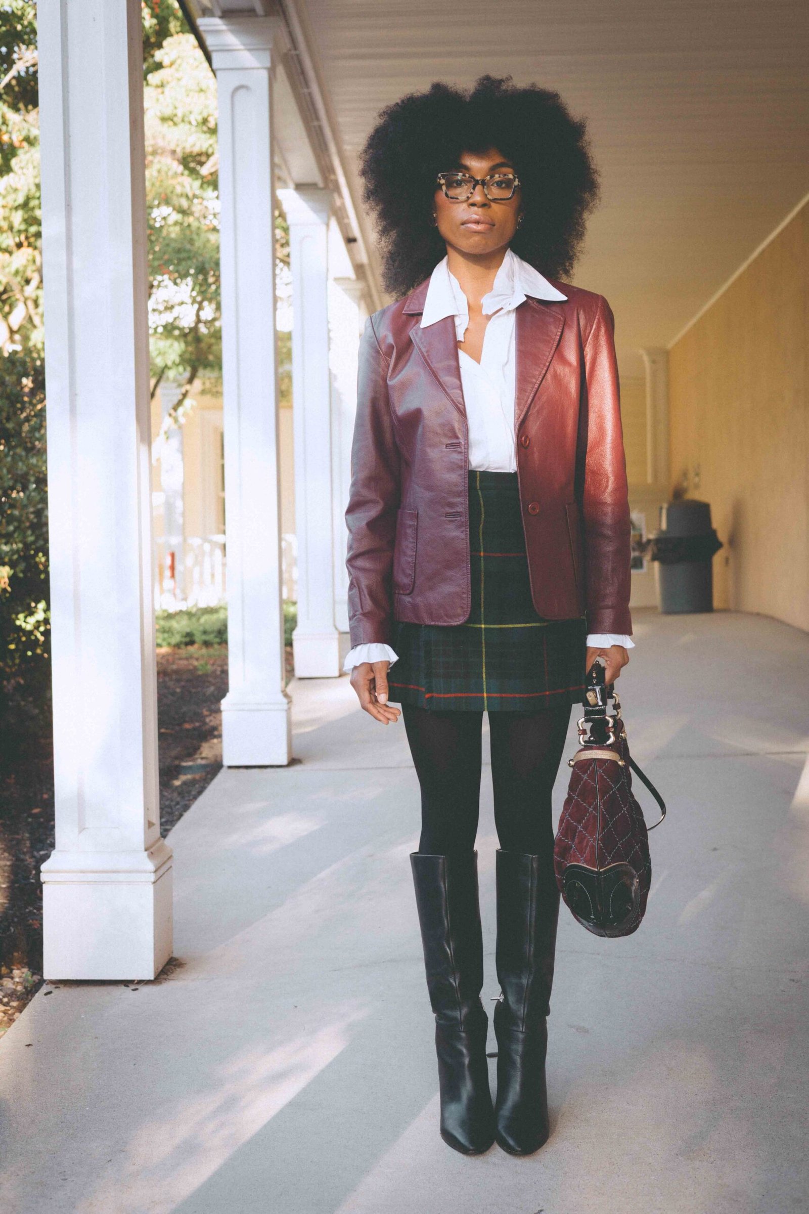 Full-length portrait of a burgundy leather blazer and Scottish plaid skirt styled with a vintage handbag